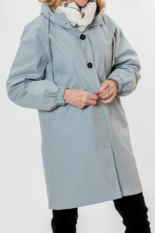 Light blue water-resistant oversized hooded windbreaker rain jacket with button closure and elastic cuffs worn with scarf and black pants